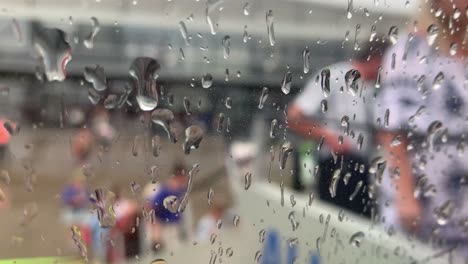 Raindrops-gently-slide-and-glide-across-the-airplane-window,-blurring-the-view-outside,-with-unrecognizable-figures-in-the-background-adding-a-serene,-atmospheric-effect