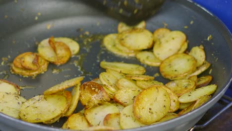 Crispy-Potatoes-with-Seasoned-Herbs-de-Provence-and-Olive-Oil-Being-Turned-in-Very-Hot-Frying-Pan-Being-Cooked-Outside-on-Summer-Evening-4K