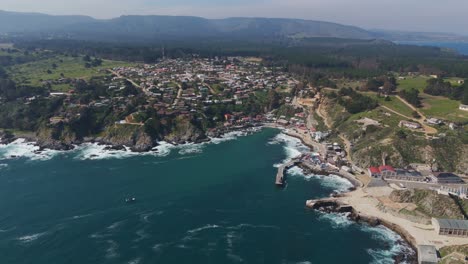 Aerial-view-showcasing-the-coastal-fishing-village-of-Caleta-Quintay-in-Paine,-Santiago-Metropolitan-Region,-Chile,-perched-on-rugged-cliffs-with-waves-crashing-below