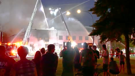 People-watch-firefighters-control-building-fire-with-water-from-fire-trucks-at-night-on-street-in-Montreal,-Quebec