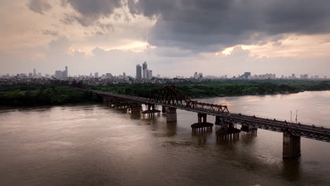 Verkehr-Auf-Der-Long-Bien-Brücke-Mit-Der-Skyline-Von-Hanoi-Im-Hintergrund-Unter-Dem-Sonnenuntergangshimmel,-Drohnenaufnahme