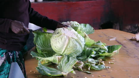 Hands-chopping-large-cabbage-with-a-knife-on-a-wooden-table-for-meal-preparation