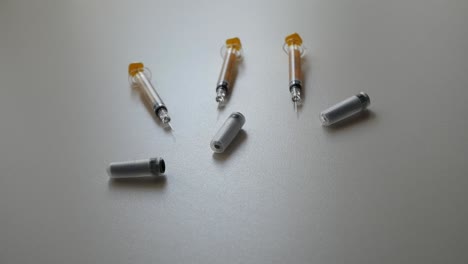 Syringes-and-container-on-white-surface-in-dynamic-lighting