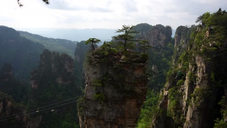 Cable-cars-move-behind-a-towering-sandstone-pillar-in-Huangshi-Village,-China