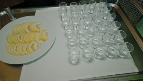 Tray-of-arranged-lemon-slices-beside-a-set-of-empty-shot-glasses-on-a-white-cloth