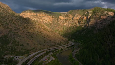 Summer-Glenwood-Canyon-Scenic-Drive-Glenwood-Springs-Colorado-River-interstate-i70-highway-west-east-car-traffic-sun-on-Grand-Mesa-late-afternoon-dark-rain-thunderstorm-clouds-forward-pan-up-motion