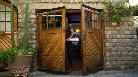 Young-male-with-work-papers-walking-through-double-wooden-doors-into-an-office-space