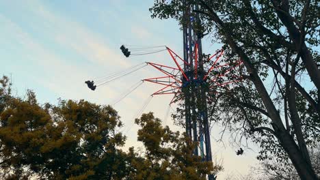 Amusement-park-game,-colorful-spinning-high-chairs-in-the-middle-of-trees,-sunset-in-the-background