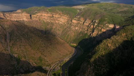 Summer-Glenwood-Canyon-Scenic-Drive-Glenwood-Springs-Colorado-River-interstate-i70-highway-west-east-car-traffic-sun-on-Grand-Mesa-cliffside-late-afternoon-dark-rain-thunderstorm-cloud-backward-pan