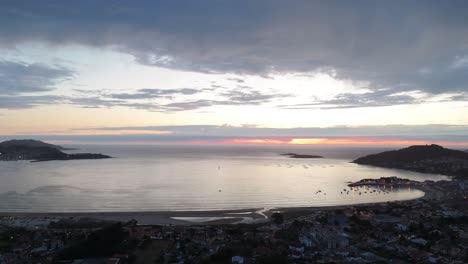 Aerial-sunset-view-over-Baiona's-Playa-América,-Spain,-with-glowing-horizon-and-calm-sea-waters