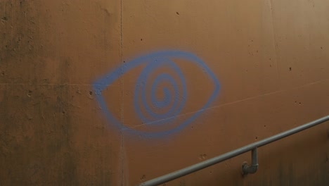 Blue-spiral-eye-graffiti-on-a-weathered-concrete-wall-near-a-metal-railing