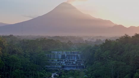 Indonesia-landscape-with-mountain-silhouette-and-waterfall-during-sunrise,-aerial-view