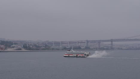 Fähre-Gleitet-über-Den-Tejo-In-Lissabon-An-Einem-Bewölkten-Tag,-Brücke-Im-Hintergrund