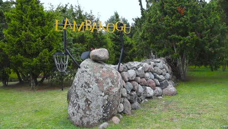 A-stone-lamb-or-sheep-sculpture-in-Saaremaa-near-a-traditional-stone-wall-holding-up-a-sign-that-says-Lambakogu,-a-popular-tourist-attraction-site-in-Estonia