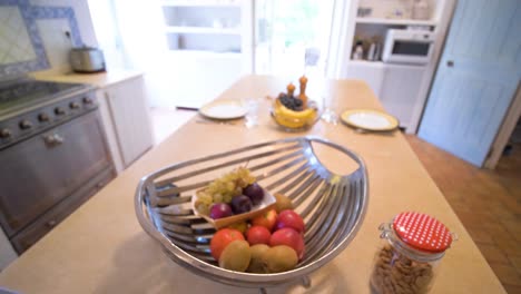 A-dining-table-adorned-with-fruits-in-a-metal-bowl,-set-within-the-cozy-interior-of-a-household-at-Maison-Goult,-France