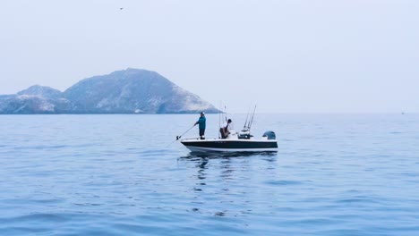 Aerial-centered-orbit-of-a-fishing-boat-near-the-rocky-shores-of-Coronado-Islands,-Mexico,-under-a-hazy-sky