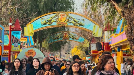 Establishing-a-large-group-of-people-passing-through-the-arches-of-the-Fantasilandia-amusement-park-in-Santiago-de-Chile,-sunny-day