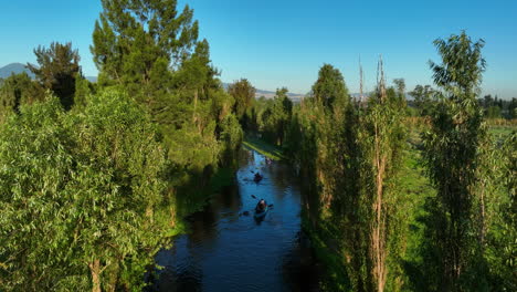 Aerial-view-tracking-people-paddling-through-a-narrow-river-in-Xochimilco,-Mexico