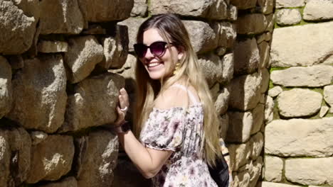 Blonde-woman-with-sunglasses-laughs-leaning-on-stone-wall-in-Machu-Picchu-lost-city-archaeological-ruins