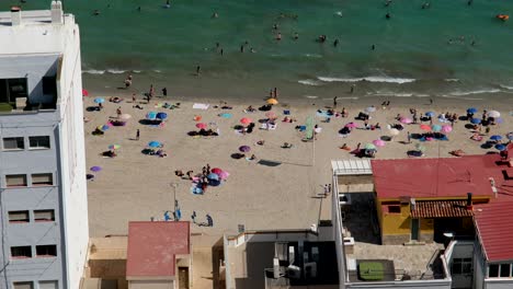 Alicante’s-beach-is-packed-with-people-soaking-up-the-sun,-enjoying-the-hot-summer-day,-vibrant-energy,-and-clear-blue-waters-along-the-coast