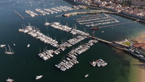 Vista-Aérea-Del-Puerto-Deportivo-De-Baiona-Con-Filas-De-Barcos-Atracados,-Aguas-Cristalinas-Y-Playa-De-Arena.