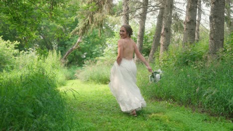 Bride-running-through-forest,-smiling-back-at-camera,-holding-bouquet-in-hand