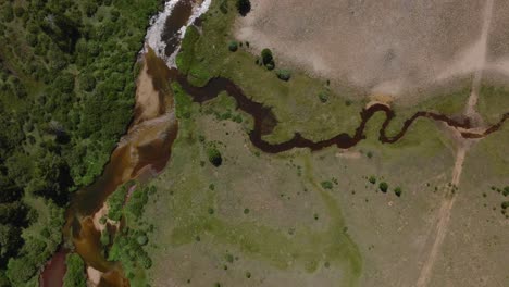 Aerial-tracking-follows-truck-on-dirt-road-over-green-plains-and-rivers-in-Wind-River-Wilderness,-Wyoming,-near-Big-Sandy-Trailhead,-with-mountain-views-in-the-distance