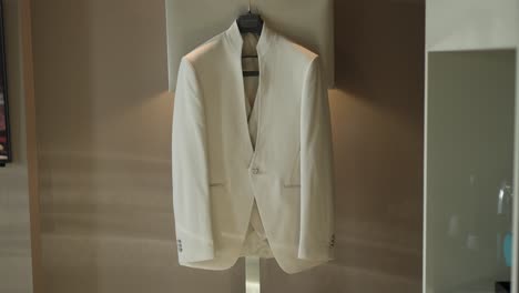 White-suit-jacket-hangs-neatly-on-a-hanger,-showcasing-sleek-and-minimal-design