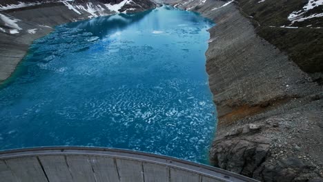 4k-Drone-Aerial-Shot-Of-Vibrant-Blue-Glacial-Water-Of-Lac-de-Moiry-Dam-Surrounded-By-Massive-Snow-Covered-Mountain-Peaks-Reflecting-On-lake-In-Grimentz-Switzerland