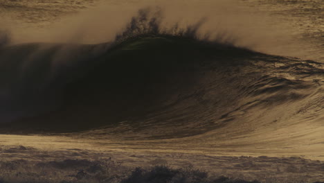 A-stunning-slow-motion-capture-of-a-wave-at-sunset,-filmed-from-the-shore,-showcasing-the-dark-silhouette-of-the-wave-against-the-glowing-horizon