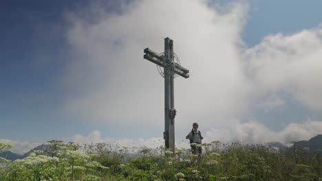 A-woman-hiking-near-a-large-cross-on-a-mountain-in-Berwang,-Austria-on-a-clear-day