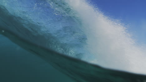 Slow-motion-shot-of-a-wave-crashing-with-great-intensity,-filmed-from-inside-the-water-at-sunrise,-showcasing-the-wave's-raw-power-and-motion