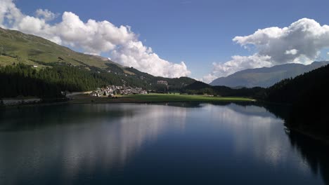 Luftaufnahme-Der-Ruhigen-Seeoberfläche-Des-Silvaplanersees-In-Graubünden,-Schweiz,-Mit-Heiterem-Wasser,-Das-Ein-Ruhiges-Wohngebiet-Entlang-Der-Uferlinie-Widerspiegelt