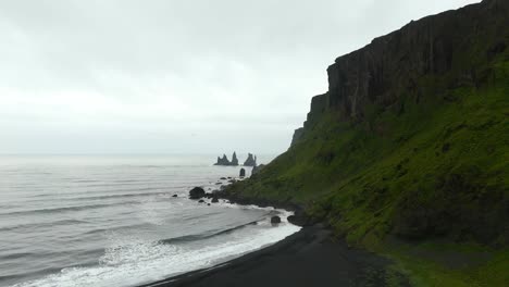 Watch-as-the-drone-showcases-Vik’s-iconic-Reynisfjara-beach,-with-its-dramatic-basalt-columns-and-crashing-waves,-creating-a-mesmerizing-dance-of-land-and-sea