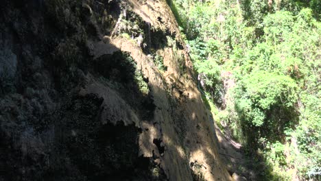 Schattige-Felsklippe-In-Der-Nähe-Der-Tumalog-Falls,-Cebu,-Mit-Sonnenlicht,-Das-Durch-Die-Bäume-Scheint