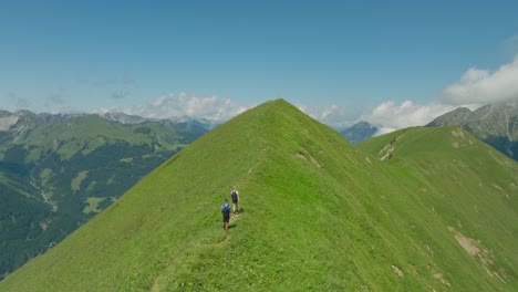 A-couple-hikes-along-a-grassy-ridge-under-a-bright-blue-sky-in-the-mountains-of-Austria