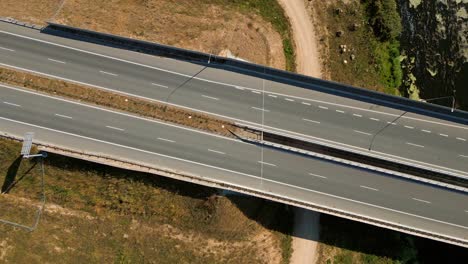 Trucks-and-cars-driving-on-river-bridge-road-expressway-highway-through-rural-landscape,-Overhead-aerial-view