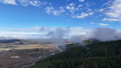 Drone-passing-through-a-cloud-near-Gura-Humorului-city,-showcasing-the-river-and-forested-trees