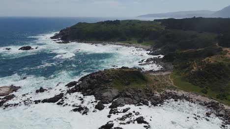 Stunning-aerial-view-capturing-the-rugged-coastline-of-Playa-Chica-in-Quintay,-Valparaíso,-Chile,-showcasing-its-dramatic-waves,-rocky-shoreline