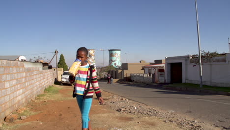 Young-children-in-Soweto-walk-up-a-township-street-with-the-iconic-Soweto-cooling-towers-in-the-background