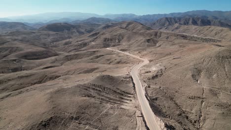 Aerial-view:-Gravel-road-cuts-through-arid-foothill-mountains-in-Peru