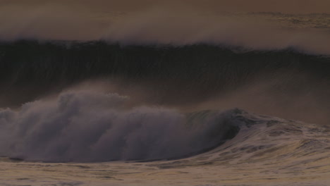 A-striking-slow-motion-capture-of-a-sunset-wave-crashing-powerfully,-filmed-from-the-shore,-highlighting-the-wave's-dark-silhouette-and-evening-light