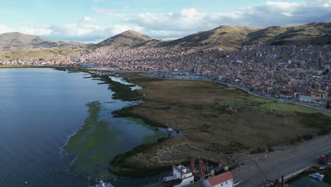 Aerial-ascends-over-Lake-Titicaca-shoreline-pier-harbour-in-Puno,-Peru