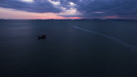 Aerial-view-over-moored-boats,-following-a-Jetski-on-the-open-sea,-dusk-in-Thailand