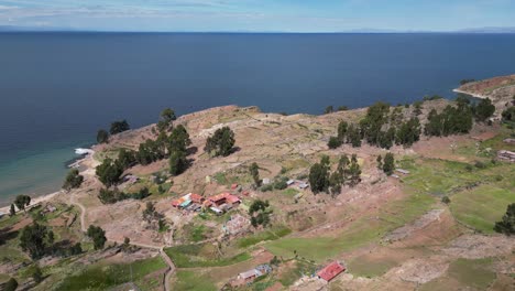 Aerial-descends-to-farmhouse-terraces-on-shore-or-Lake-Titicaca,-Peru