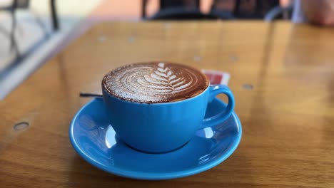 Cappuccino-coffee,-latte-art-milk-foam-design-inside-restaurant,-blue-mug