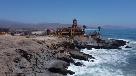 Waves-crashing-against-rocky-coastline-with-white-sandy-beach,-hotels-and-surfing