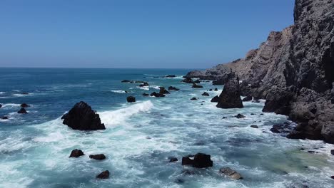 Waves-crashing-against-rocks-on-rough-coastline-with-clear-blue-water