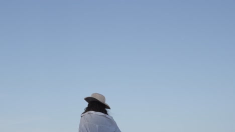 Young-Woman-girl-with-hat-and-white-shirt-on,-blue-sky-background-walking