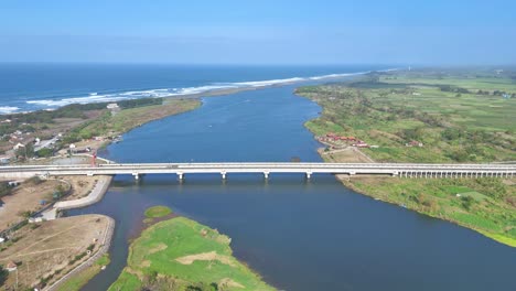 Aerial-view-of-a-white-bridge-crosses-the-river-estuary-to-the-wavy-beach